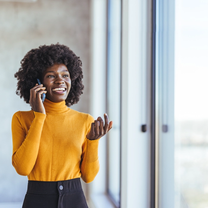 Smiling woman talking on phone near window, wearing yellow sweater Smiling woman talking on phone near window, wearing yellow sweater